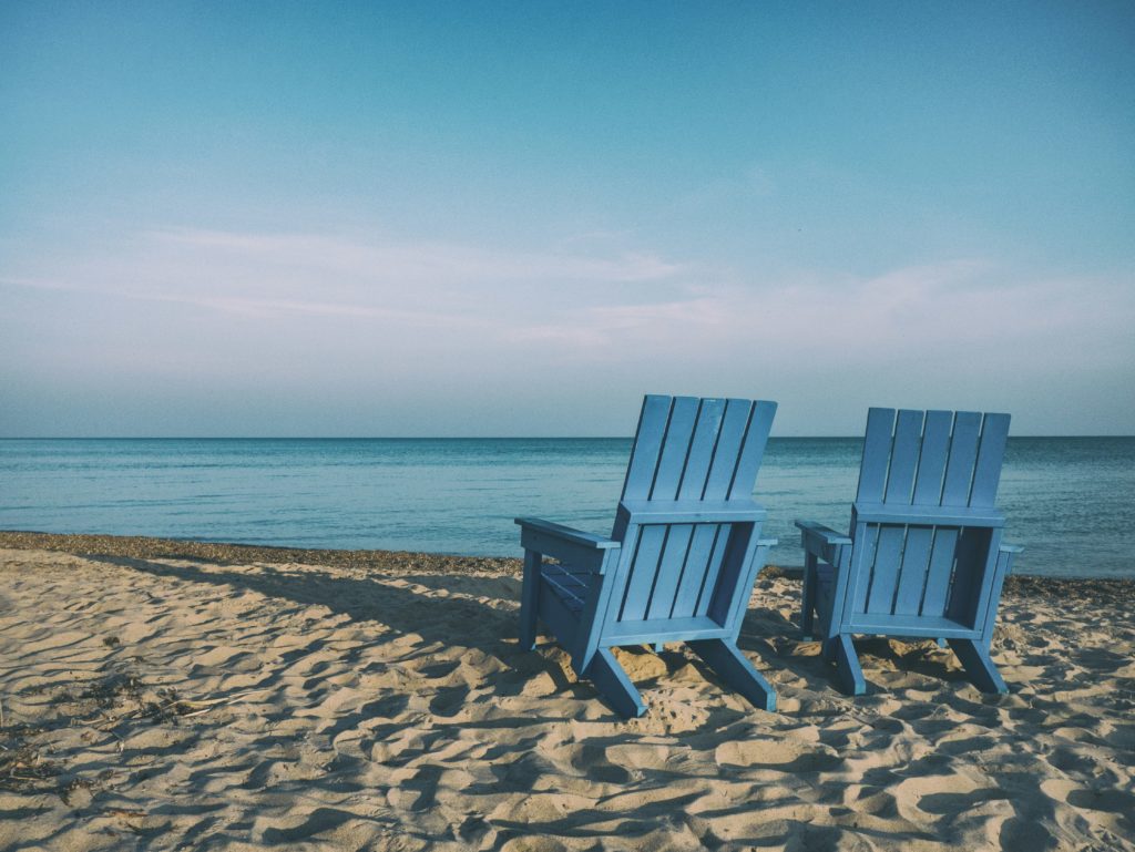 Two deck chairs on a sandy beach with blue sky's
